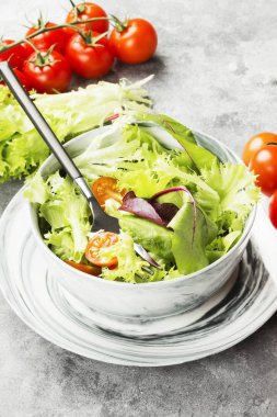 Diyet karışık yeşillik salatası (mesclun, mache, marul) ve hafif bir arka plan üzerine bir kase kiraz domates