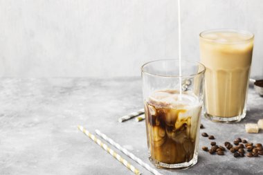 Buz gri bir arka plan üzerinde uzun bir bardak kahve dökülen süt.