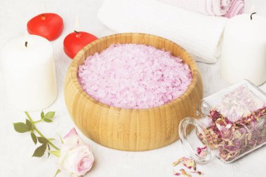 Banyo tuzu ile ahşap bir kase, yaprakları ve taze bir pembe Gül gül kokusu, havlu ve beyaz zemin üzerine mumlar. Tonlama