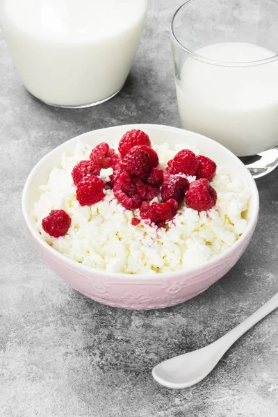 Cottage cheese in bowl with frozen raspberry and milk in glass on a light background