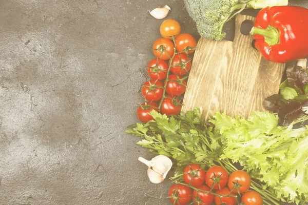 Surtido de verduras frescas (pimienta, tomates cherry, cebollas, ajo, espinacas) sobre un fondo oscuro. Tabla de cortar de madera. Vista superior, espacio de copia. Fondo alimenticio. Tonificación — Foto de Stock