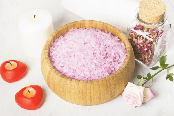 Sal de baño con aroma a rosa en un cuenco de madera, pétalos y rosa fresca, toallas y velas sobre fondo blanco. Tonificación — Foto de Stock