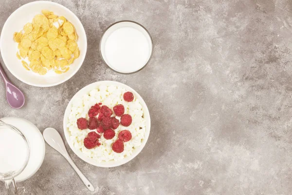 Cottage cheese in bowl with frozen raspberry and cup of cornflak