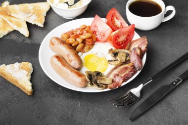 Geleneksel İngiliz kahvaltısı - pastırma, sosis, sahanda yumurta, domates, fasulye, mantar, tereyağı - beyaz plaka ve karanlık bir arka plan üzerine kahve ile tost