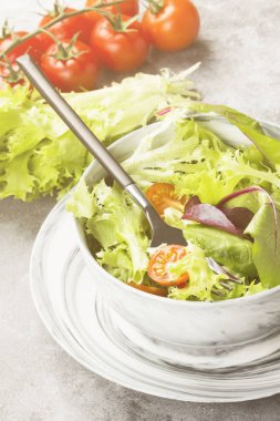 Diyet karışık yeşillik salatası (mesclun, mache, marul) ve hafif bir arka plan üzerine bir kase kiraz domates. Tonlama