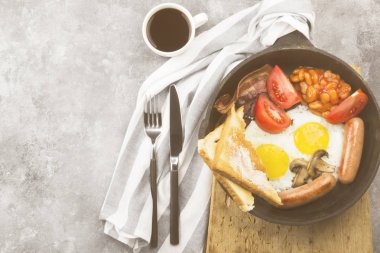 Geleneksel İngiliz kahvaltısı - pastırma, sosis, sahanda yumurta, domates, fasulye, mantar, tereyağı tava ve gri arka plan üzerinde kahve pişirme ile-tost. Görünümü en çok, uzay kopyalayın. Gıda arka plan. Tonlama