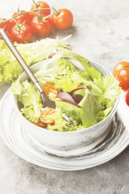 Diyet karışık yeşillik salatası (mesclun, mache, marul) ve hafif bir arka plan üzerine bir kase kiraz domates. Tonlama