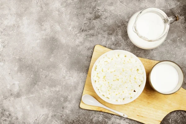 Ahşap kesme tahtası ve süt hafif bir arka plan üzerinde cam kase süzme peynir. Görünümü en çok, uzay kopyalayın. Gıda arka plan