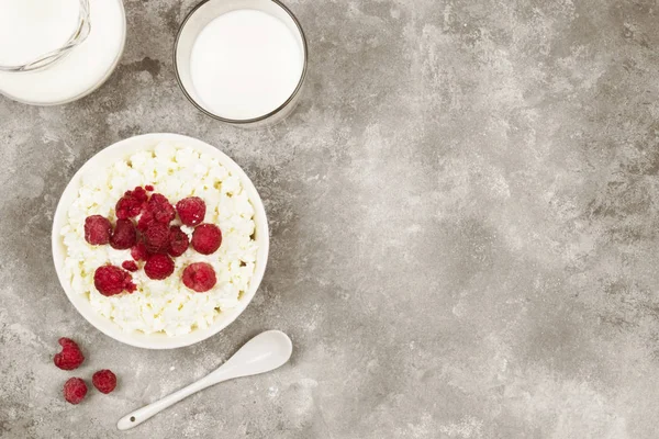 Cottage cheese in bowl with frozen raspberry and milk in glass on a light background. Top view, copy space. Food background. Toning