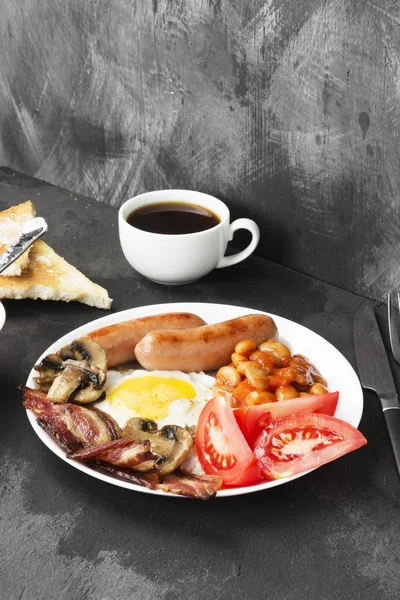 전통적인 영국식 아침 식사-베이컨, 소시지, 달걀 프라이, 토마토, 콩, 버섯, 버터-흰색 접시에 어두운 배경에서 커피와 토스트 — 스톡 사진