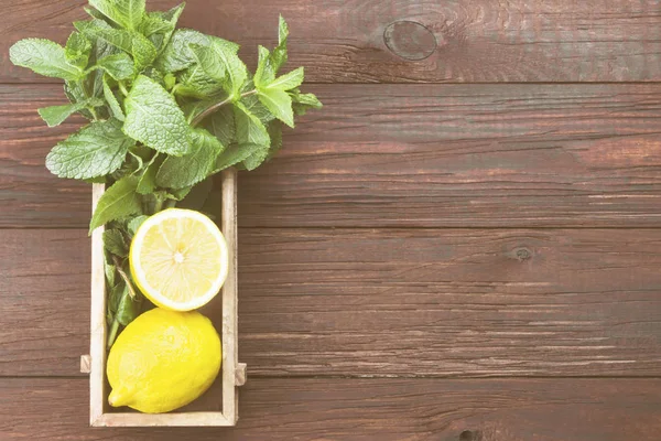 Ingredients for lemonade - lemon, mint in wooden box on a wooden background. Top view, copy space. Food background. Toning