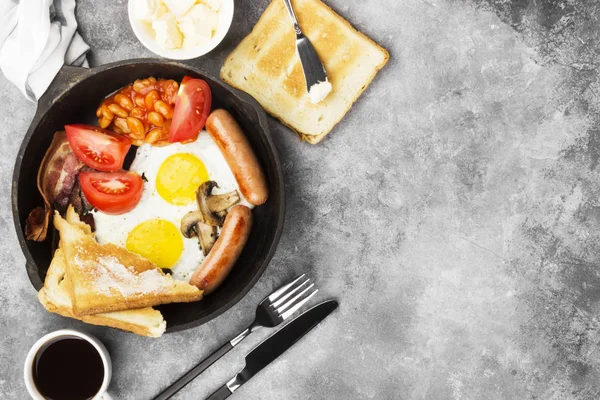 传统的英国早餐-培根, 香肠, 煎蛋, 西红柿, 豆类, 蘑菇, 烤面包用 butter-in 烹饪锅和咖啡的灰色背景。顶部视图, 复制空间。食品背景 — 图库照片
