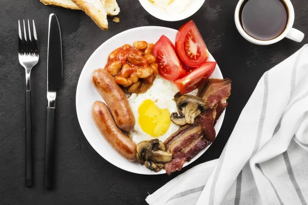 传统的英国早餐-培根, 香肠, 煎蛋, 西红柿, 豆类, 蘑菇, 烤面包用 butter-in 白盘子和咖啡在黑暗的背景。顶部视图。食品背景 — 图库照片