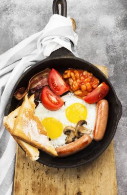 Geleneksel İngiliz kahvaltısı - pastırma, sosis, sahanda yumurta, domates, fasulye, mantar, tereyağı tava ve gri arka plan üzerinde kahve pişirme ile-tost. Üstten Görünüm. Gıda arka plan