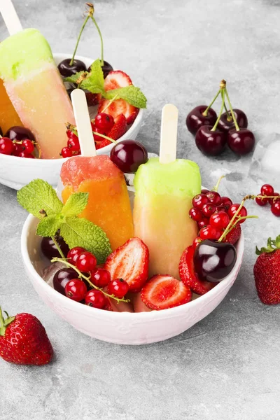 Mehrfarbige Eis am Stiel mit Erdbeere, roter Johannisbeere und Kirsche auf grauem Hintergrund — Stockfoto