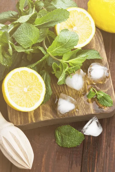 Los ingredientes para la limonada - el limón, la menta, el hielo sobre la tabla de cortar de madera sobre el fondo de madera. Tonificación — Foto de Stock