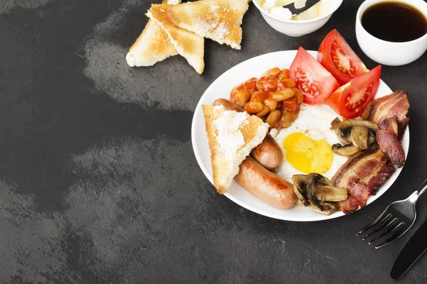 Traditional English breakfast - bacon, sausages, fried eggs, tomatoes, beans, mushrooms, toast with butter -  in white plate and coffee on a dark background. Top view, copy space. Food background — Stock Photo, Image