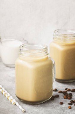 Buz gri bir arka plan üzerinde uzun bir bardak sütlü kahve. Tonin