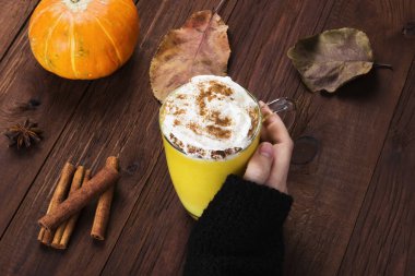 Siyah kazaklı bir fincan sütlü balkabağı tutan el kadın 