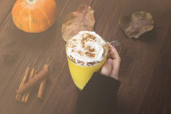 Woman hand in black sweater holding a cup of pumpkin latte with — Stock Photo, Image