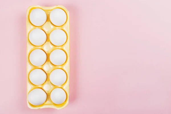 White eggs in yellow container for eggs on pink background. Top — Stock Photo, Image