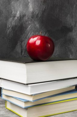 Çeşitli kitaplar ve koyu arka plan üzerinde kırmızı elma yığını