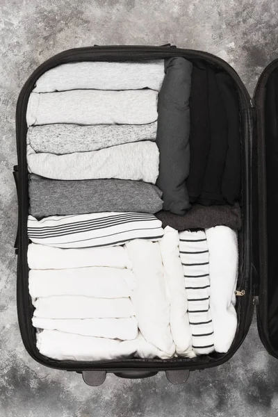 Embalaje de ropa monocromática en maleta negra. Vista superior — Foto de Stock