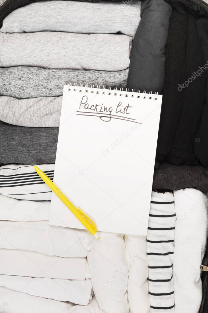 Packing of monochrome clothes in black suitcase. Packing list in