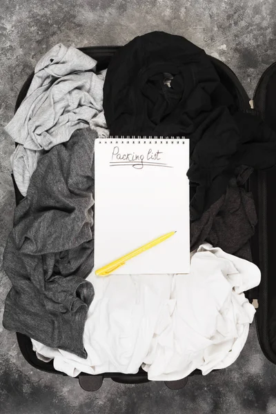 Embalagem de roupas monocromáticas em mala preta. Lista de embalagem em — Fotografia de Stock