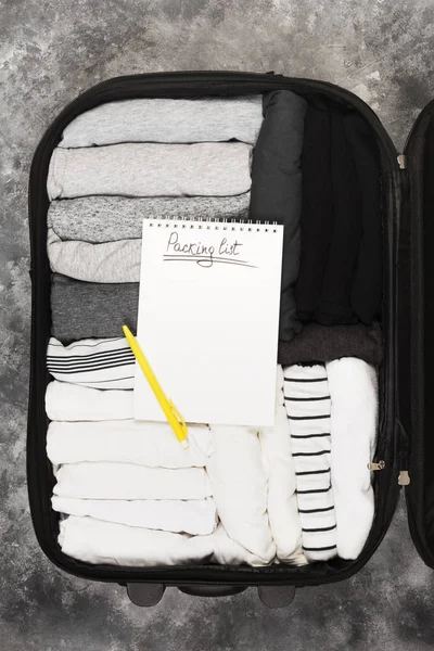 Emballage de vêtements monochromes dans une valise noire. Liste d'emballage dans — Photo
