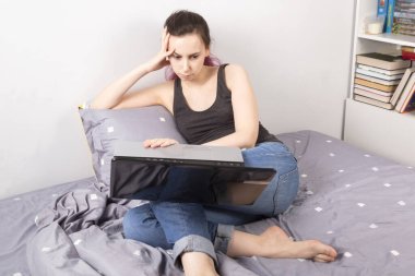 Konsept: Evden çalışma, kendini izole etme, karantina. Genç kız yatakta oturuyor, dikkatle dizüstü bilgisayarına bakıyor.