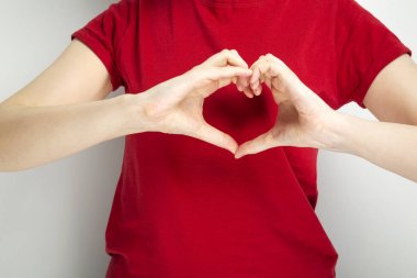 Kırmızı tişörtlü genç kız ellerini gri arka planda gösteriyor.