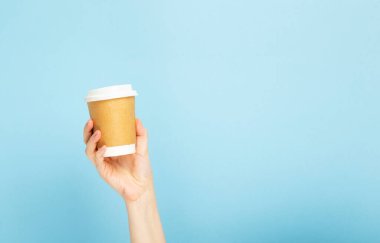 Kadının elinde mavi arka planda kahve olan bir kağıt bardak var. Boşluğu kopyala