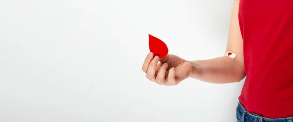 Kan bağışı. Kırmızı tişörtlü genç kız elinde tutuyor, ikinci el ise gri arka planda kan verdikten sonra kırmızı kalple bantlanmış. Boşluğu kopyala