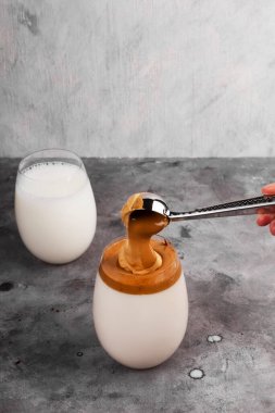 Popüler Kore Dalgon kahvesini adım adım pişiriyorum. Gri arka plandaki bir bardak süte bol köpüklü kahve, şeker ve sıcak su ekle.