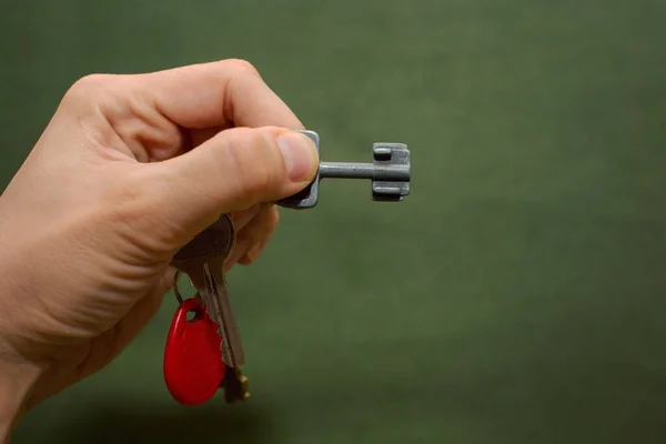 Vintage keys to the door lock in the hand of a man on a greenish background