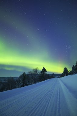 Aurora borealis over a road through winter landscape, Finnish Lapland clipart