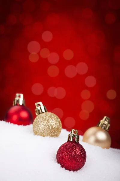 Red and gold Christmas baubles on snow, red background — Stock fotografie