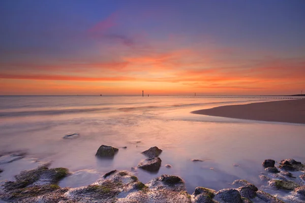 Praia com rochas ao pôr do sol em Zeeland, Países Baixos — Fotografia de Stock