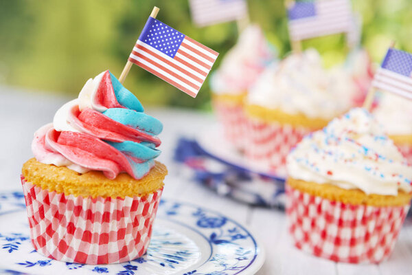 Cupcakes with red-white-and-blue frosting and American flags on an outdoor table