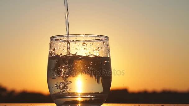 Filling glass with water at the sunset, Slow motion