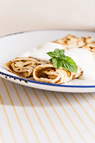 Crepes finos panqueques enrollados con crema agria menta en un plato —  Fotos de Stock