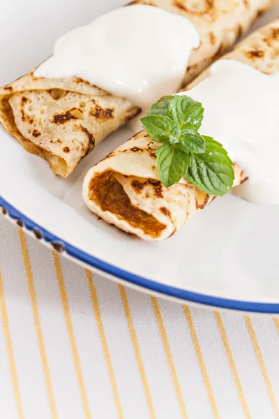 Crepes finos panqueques enrollados con crema agria menta en un plato —  Fotos de Stock