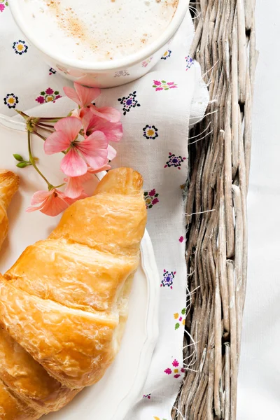 Croissants, Kaffeetasse, Blume im romantischen Stil auf einem Weidenkorb — Stockfoto