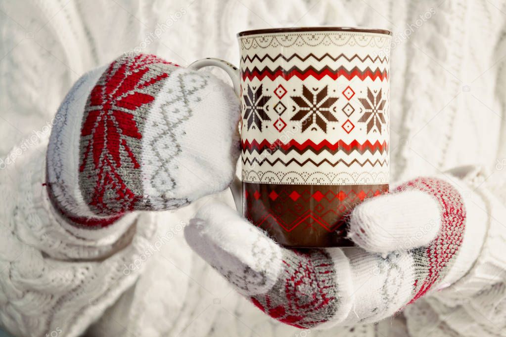 hands in mittens holding a cup of Scandinavian Christmas pattern