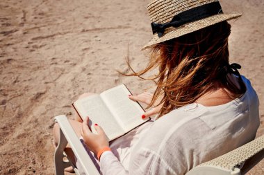 Sahilde bir kitap okuma bir şapka ile genç yetişkin kadın