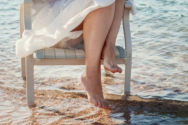 Bare legs girl in a white dress touched the sea water — Stock Photo, Image