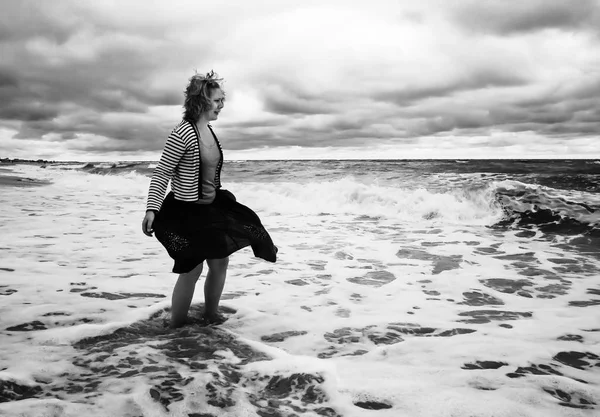 A young woman in a billowing skirt stands among the stormy sea w — Stock Photo, Image