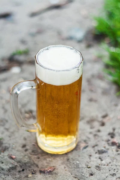 Een glas van schuimend light bier staat op de grond in een open park — Stockfoto