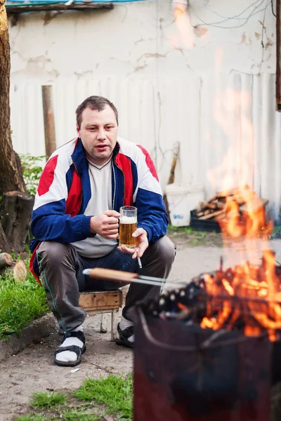 En ung vuxen man röker och dricker öl nära grillen med — Stockfoto